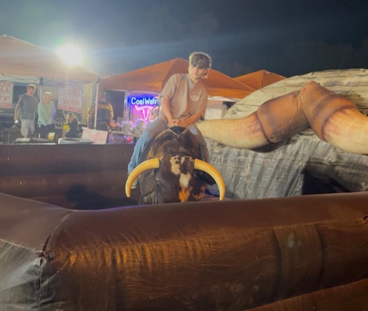 An adult rides the mechanical bull inside the orange inflatable at a night event